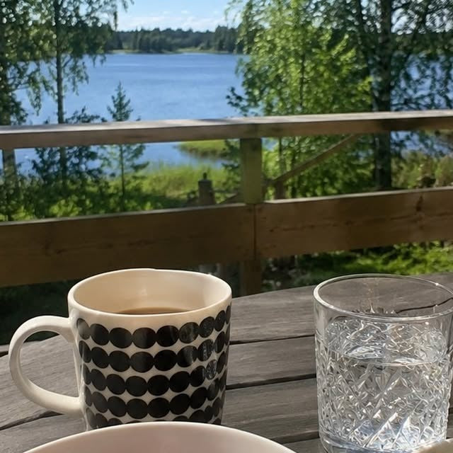 Aamukahvi ja vesilasi terassilla järven äärellä